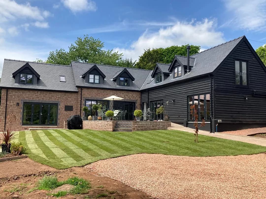 The finished extension in Monmouthshire red stone beside the timber-clad house, Usk