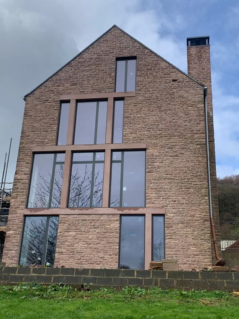A tall natural stone gable with full-height windows, by RH Stonework & Masonry