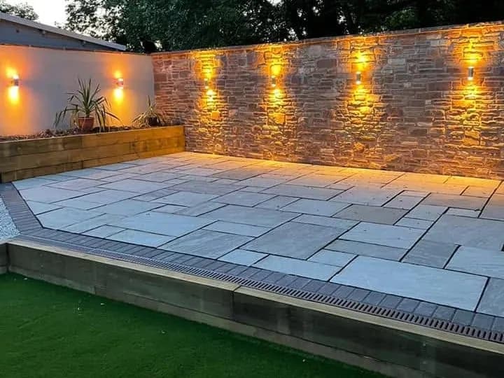 The patio at dusk, with lights washing up and down the stone wall, Monmouthshire